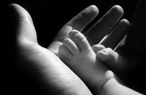 An adult hand holds a child's hand in black and white. 