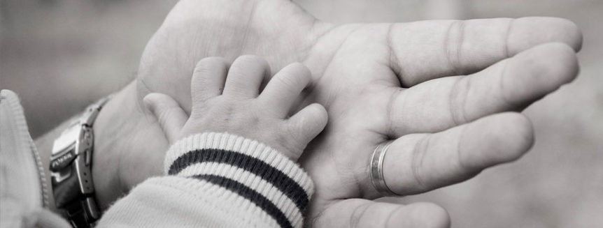 A baby's hand rests in a masculine older hand.