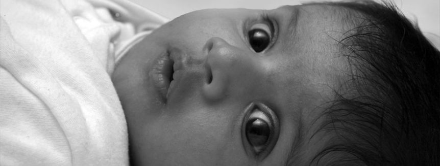 A baby with wide-open eyes stares at the camera