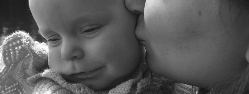 A feminine-presenting face kisses the cheek of a baby