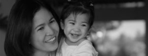 A woman of Asian descent holds her daughter in her arms, both smiling.